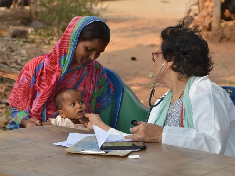 An Aarogya Vahini doctor examining a baby held by their mother during a village health checkup